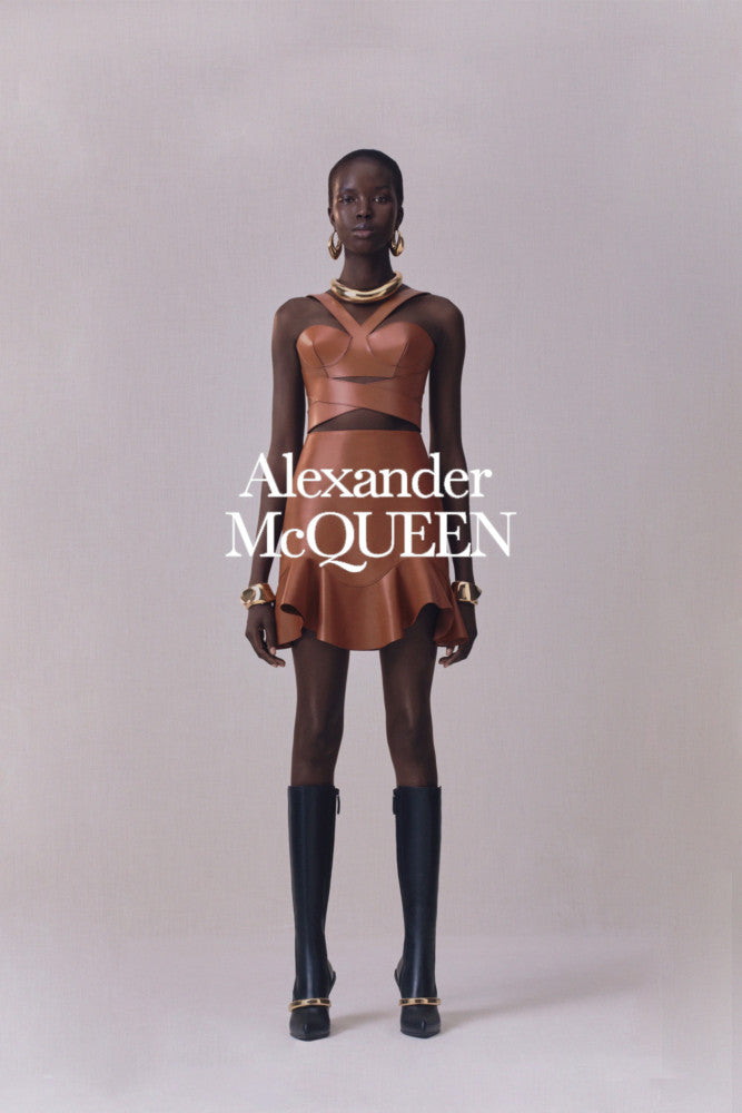 Editorial image of model wearing a leather outfit with 'Alexander McQueen' branding on a plain background