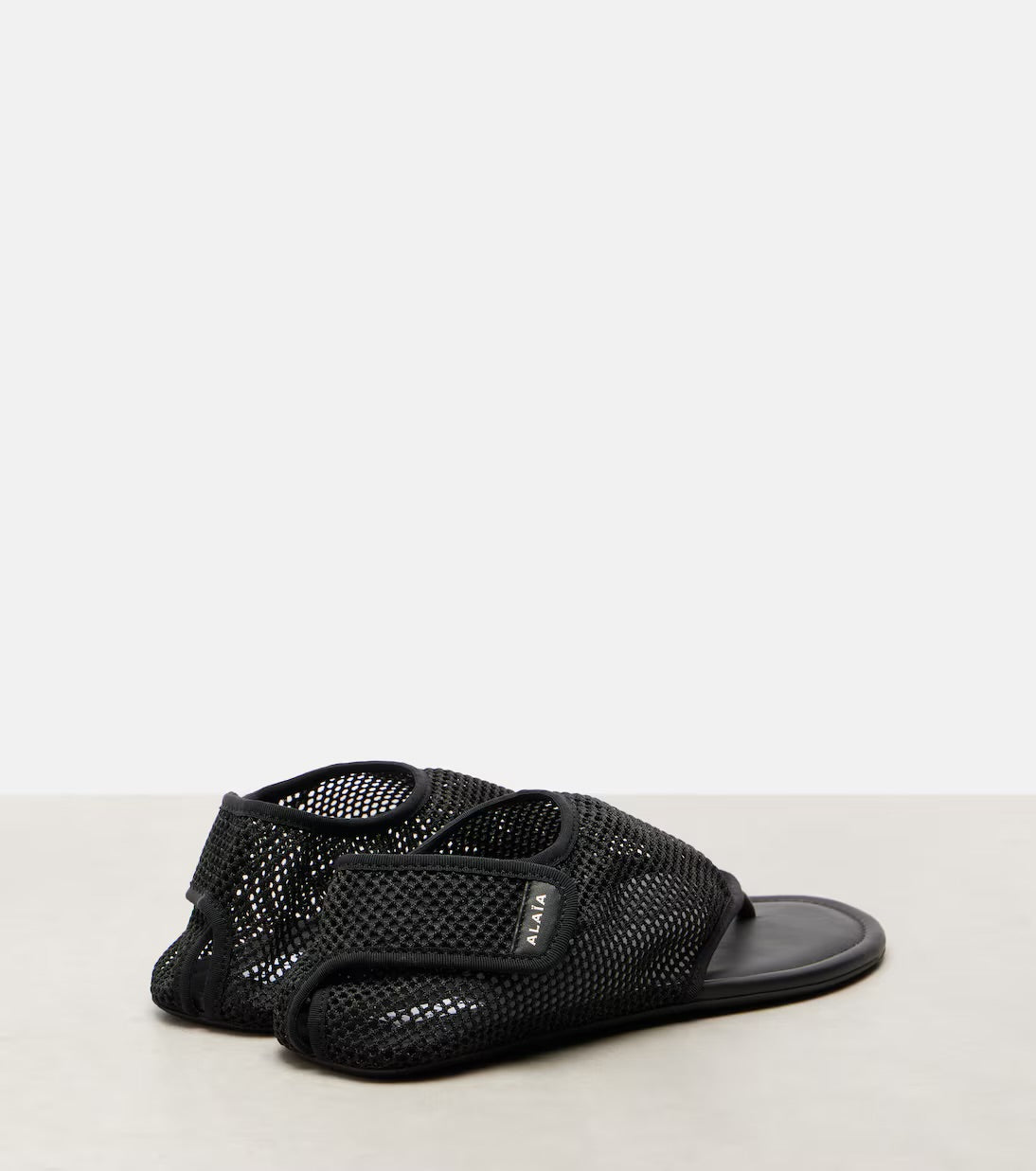 Alaia black mesh thong flat sandals product shot on grey background