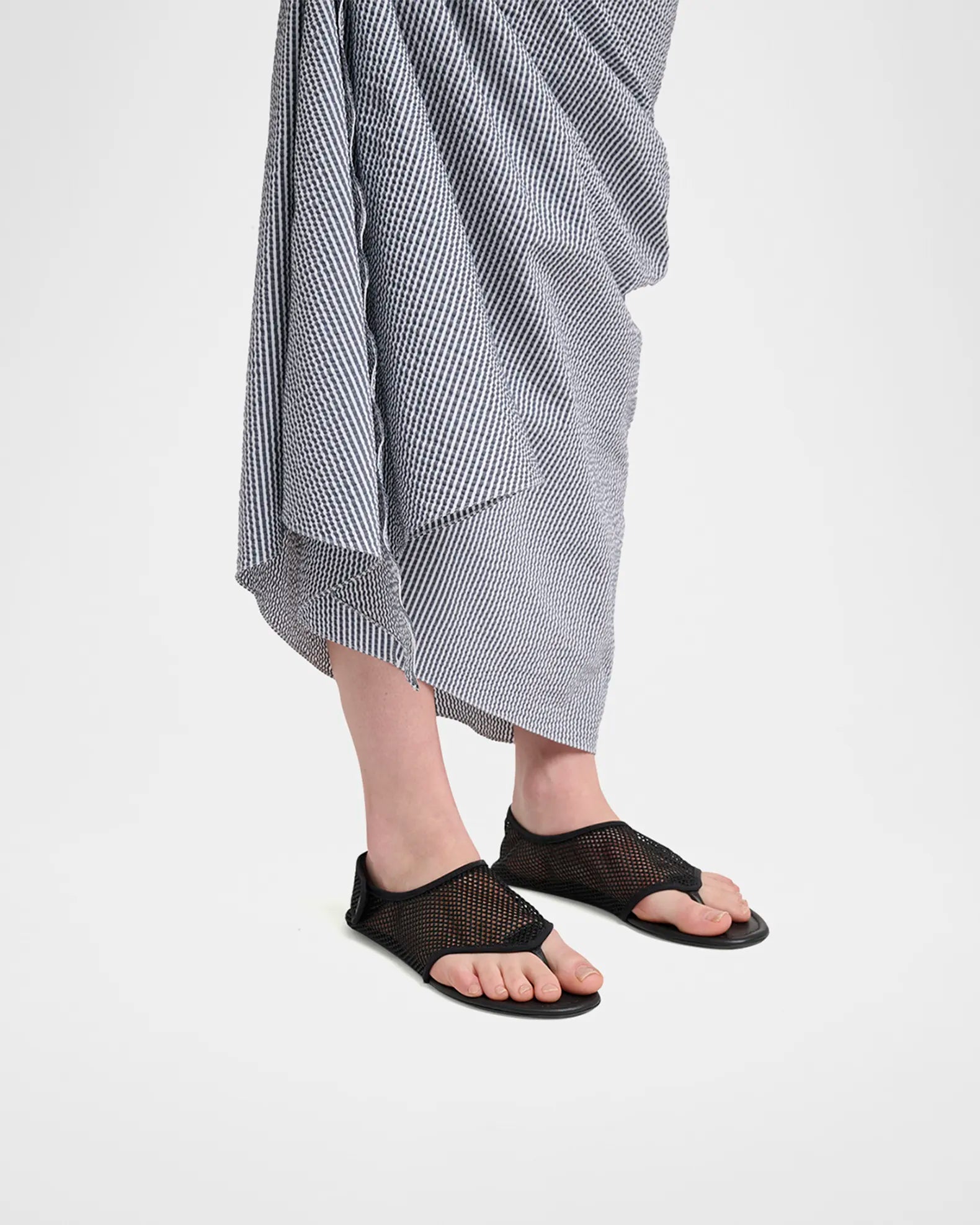 Model wearing Alaia black mesh thong flat sandals on feet