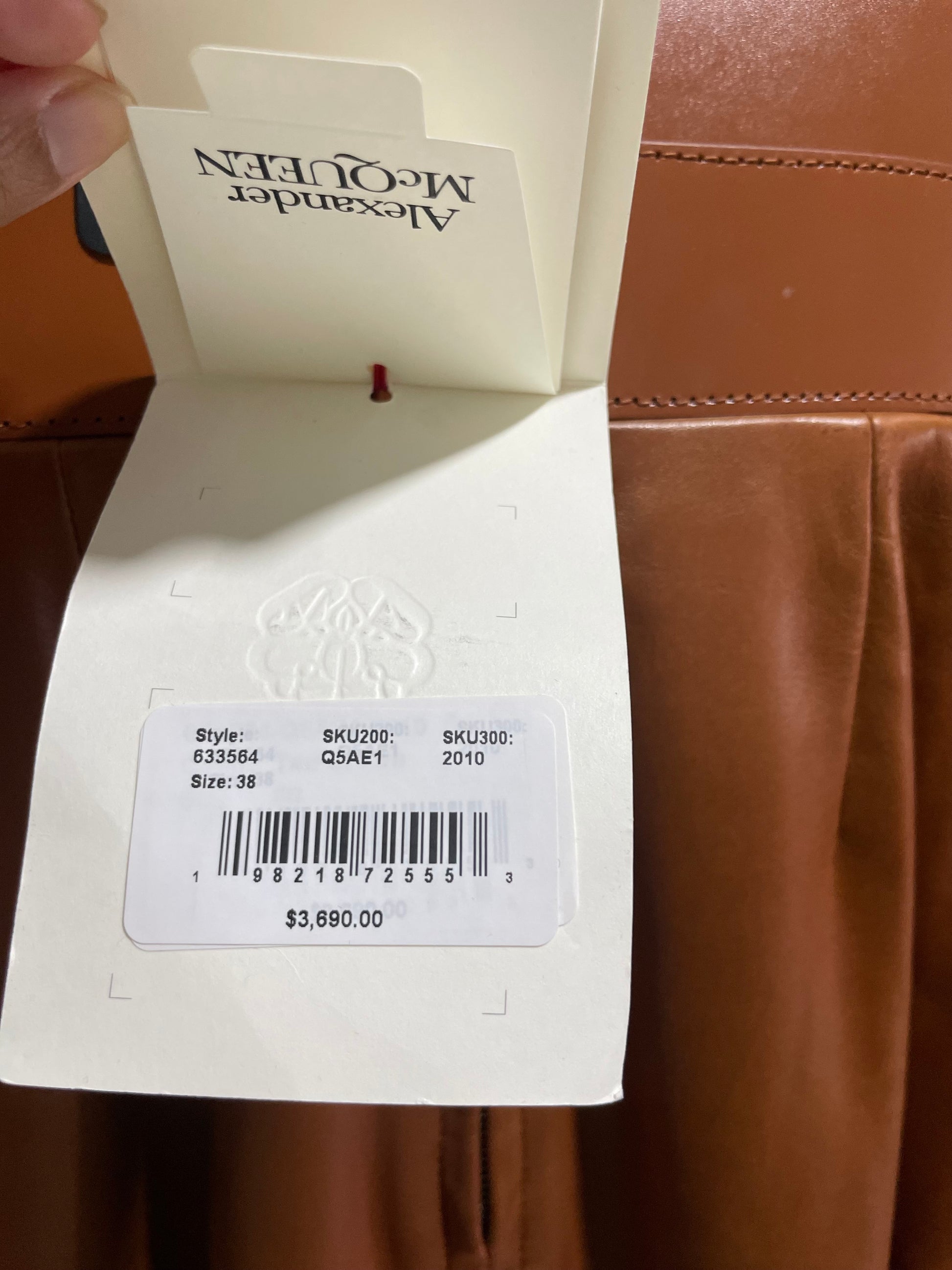 Close-up of Alexander McQueen brown leather corset dress clothing tag with brand name, retail price, and size information.