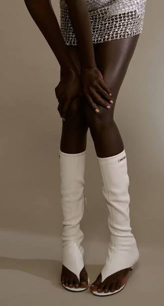 Model wearing white leather Miu Miu knee-high boots on a plain background