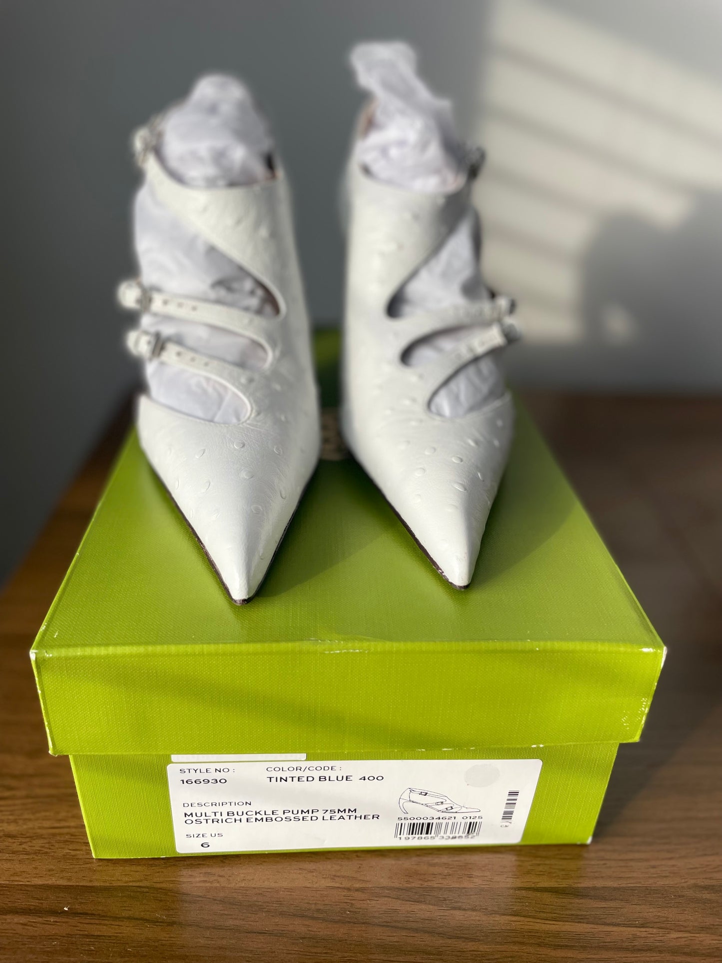 Close-up view of white Tory Burch multi-buckle pumps on green shoe box.