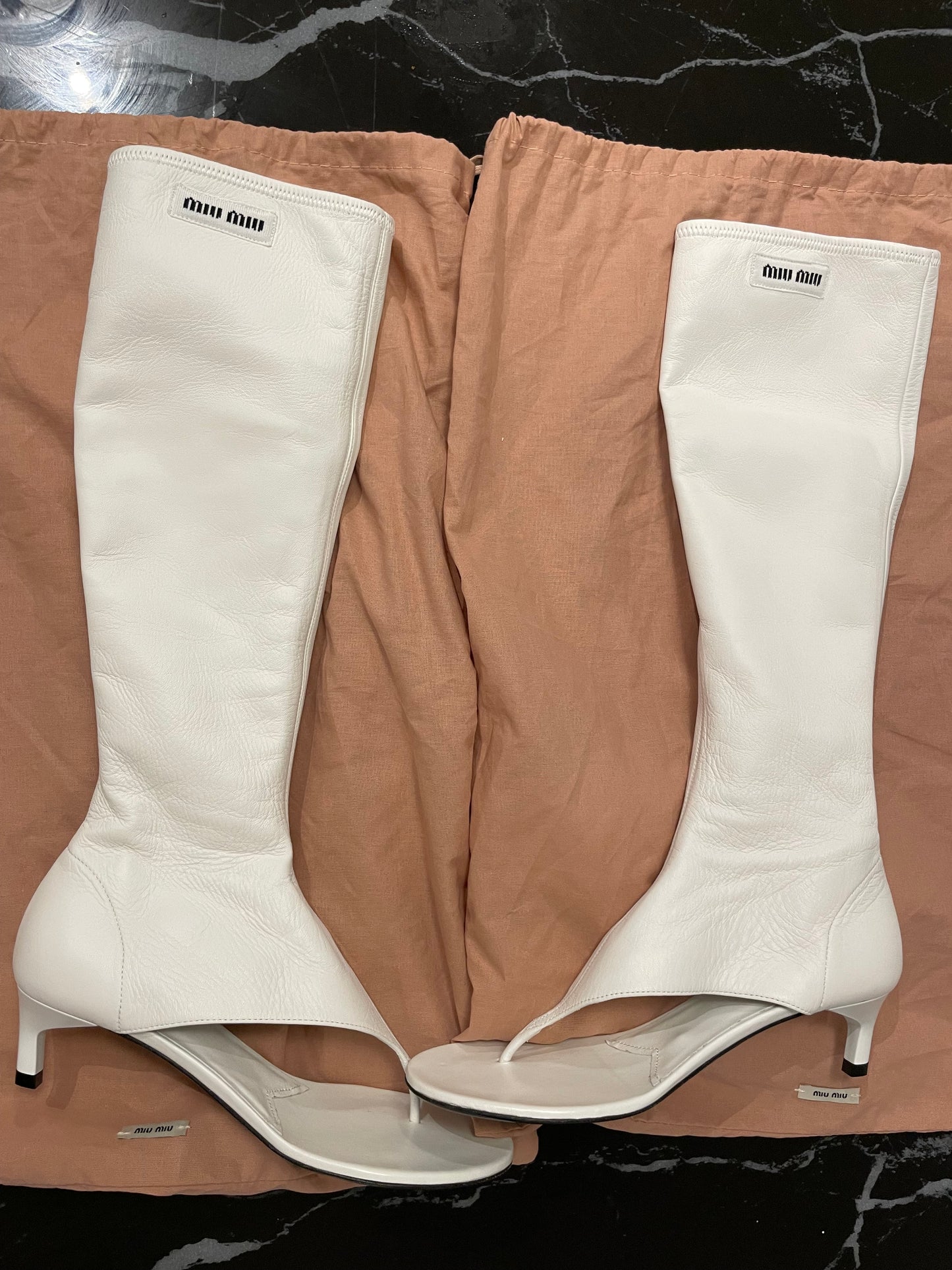 White Miu Miu thong leather sandal boots with pink dustbags on black a marble background